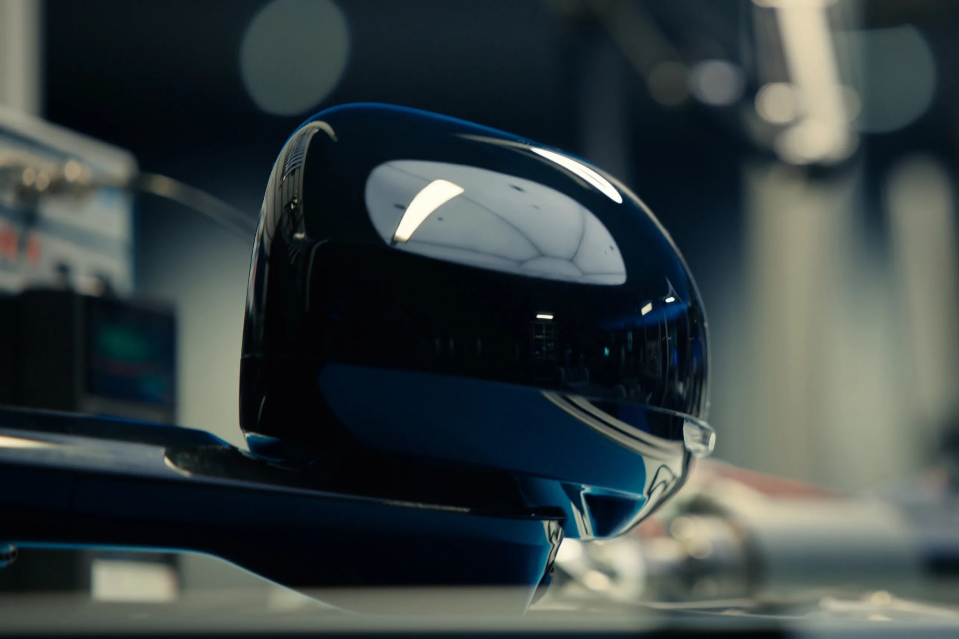 Glossy black side mirror of a car with blurred background in a workshop.