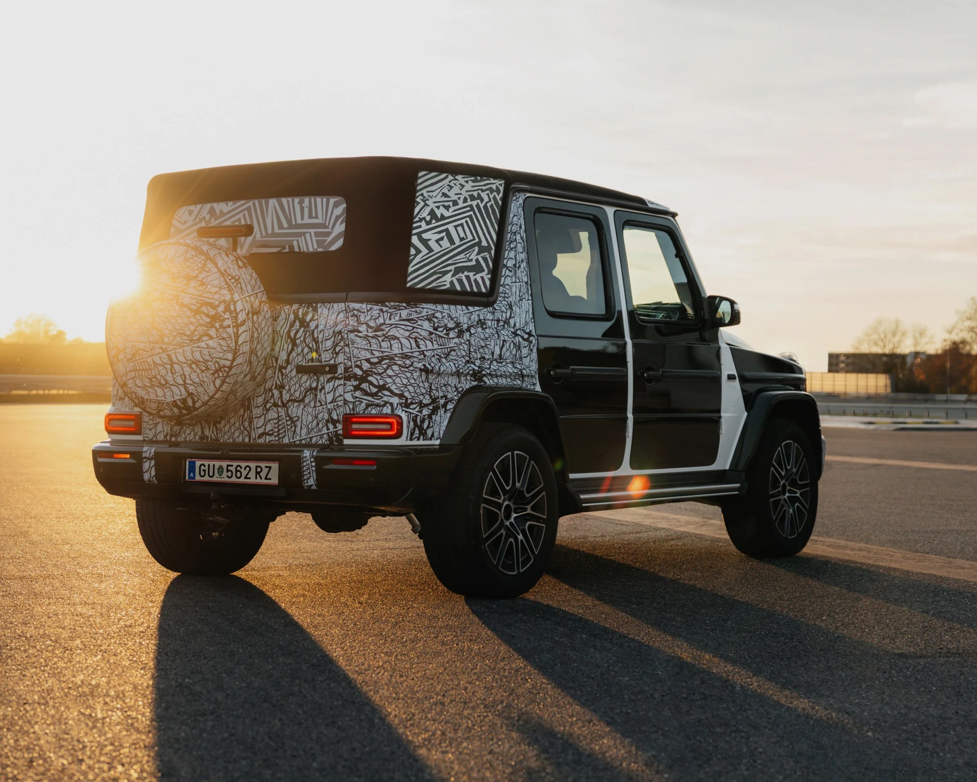 Black and white camouflaged SUV with a soft top parked on asphalt at sunset.