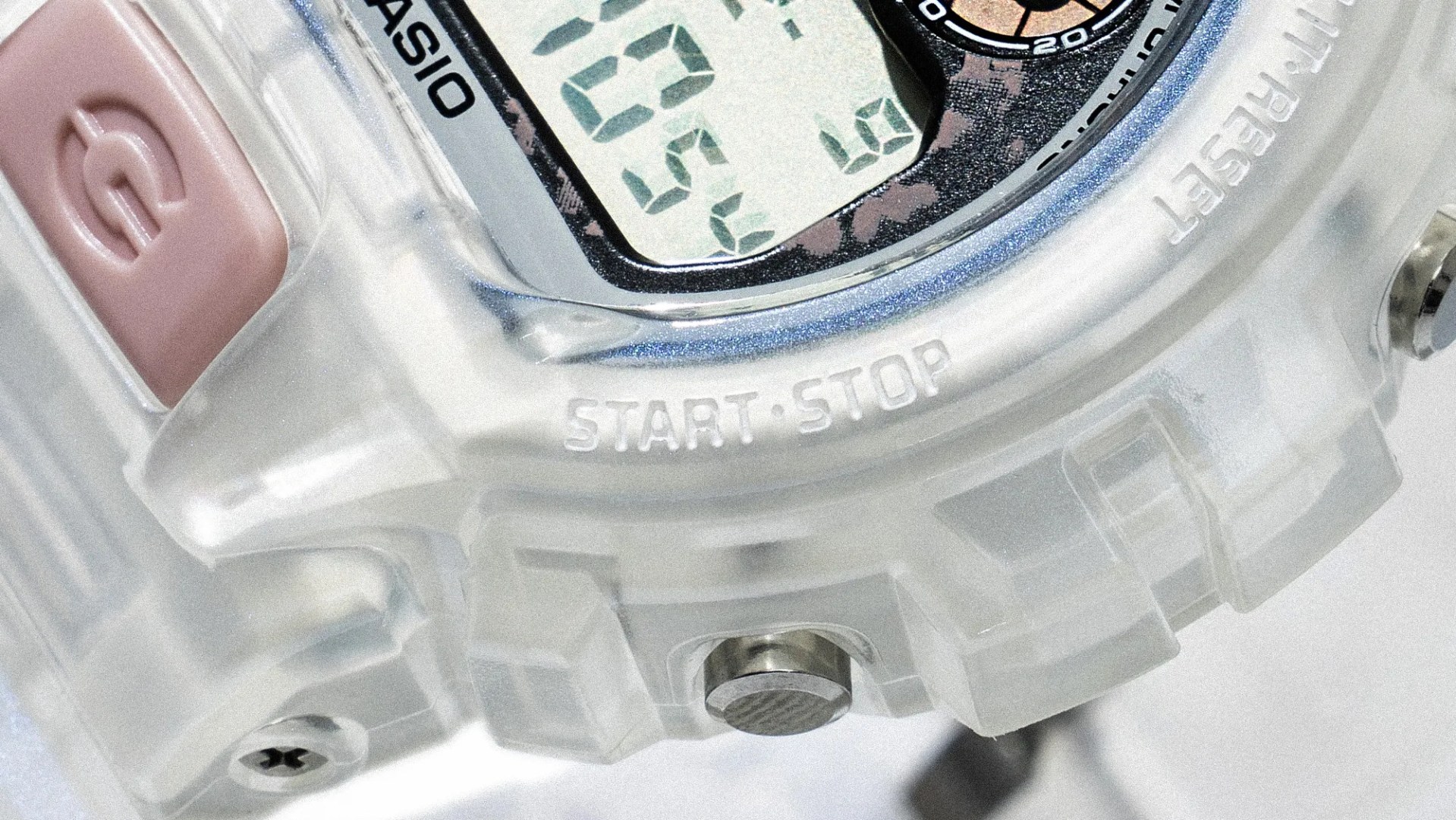 Close-up of a transparent Casio digital watch case showing a pink button and "START·STOP" text.