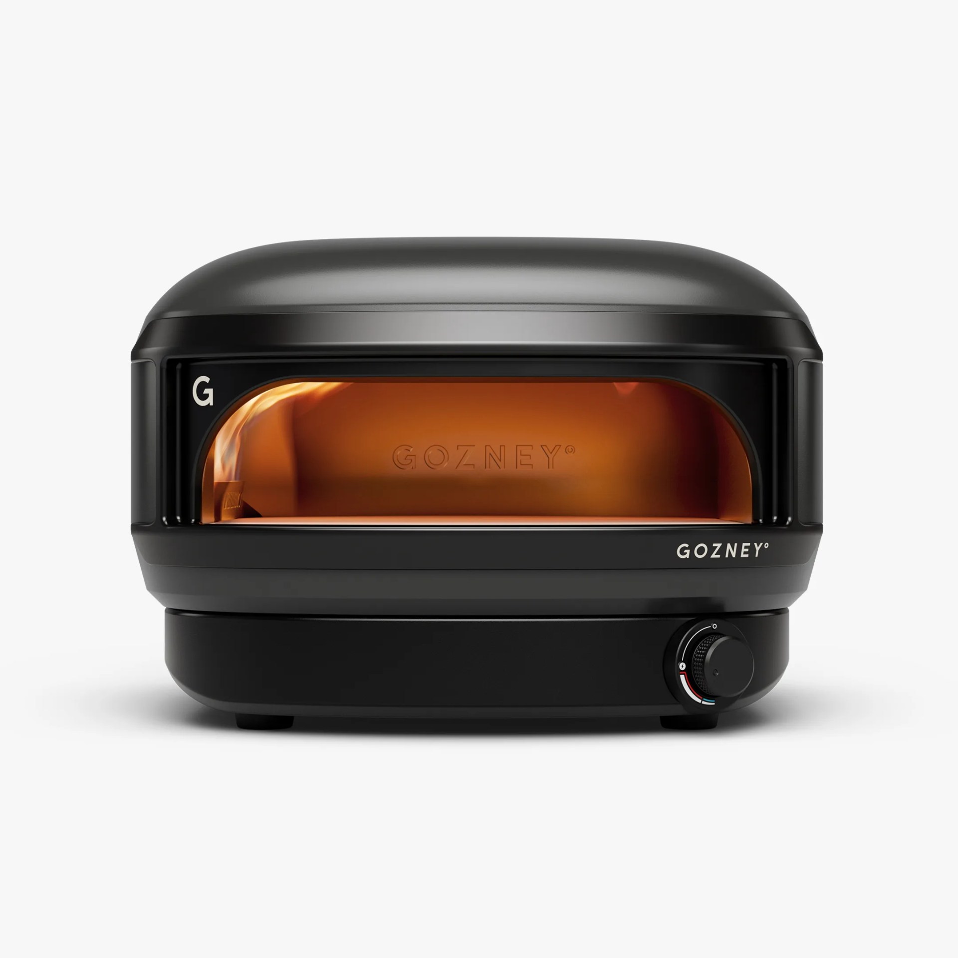 Black compact Gozney pizza oven with a visible flame inside and a temperature control knob on the front.