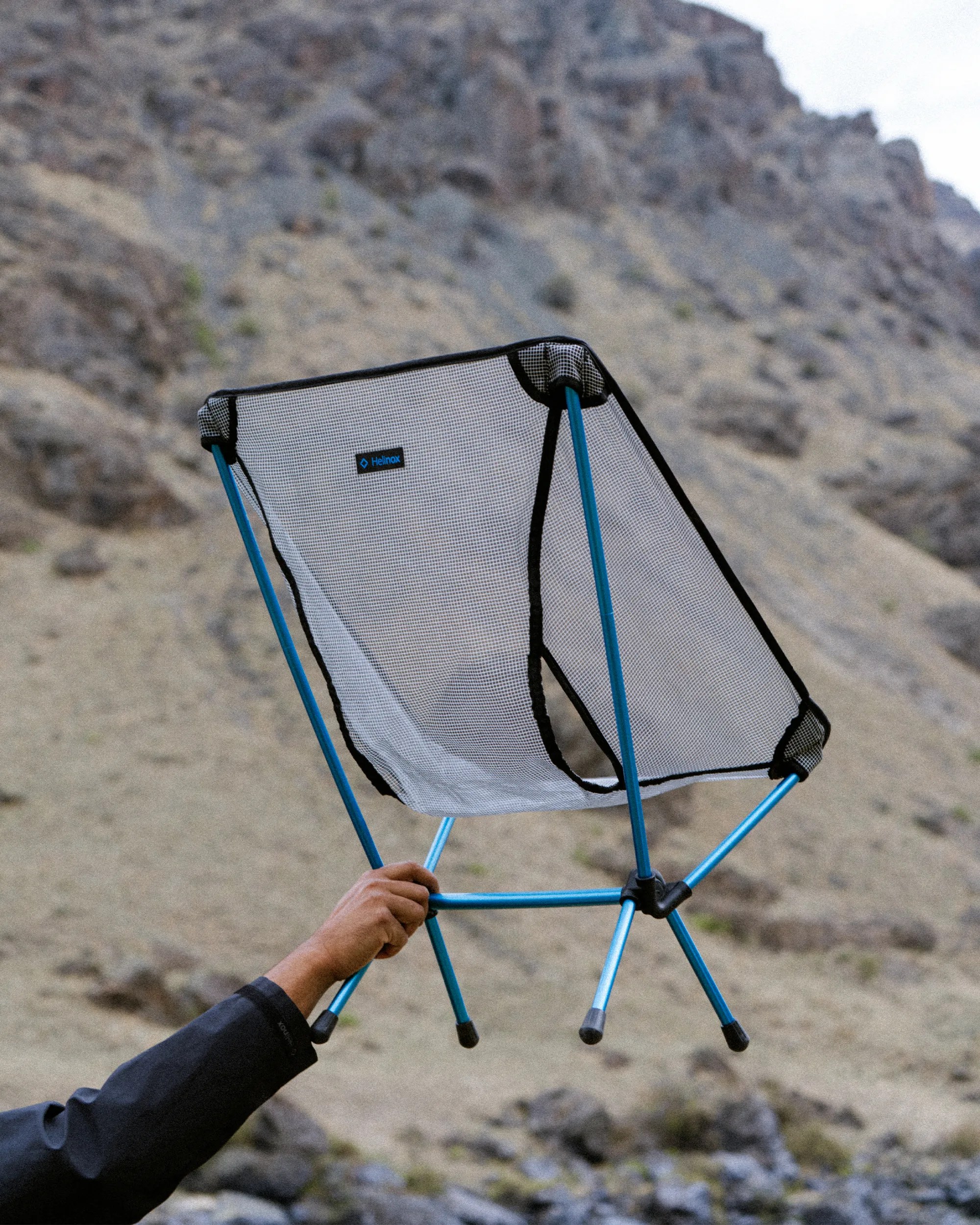 Lightweight portable camping chair with blue frame and mesh seat held by a person outdoors.