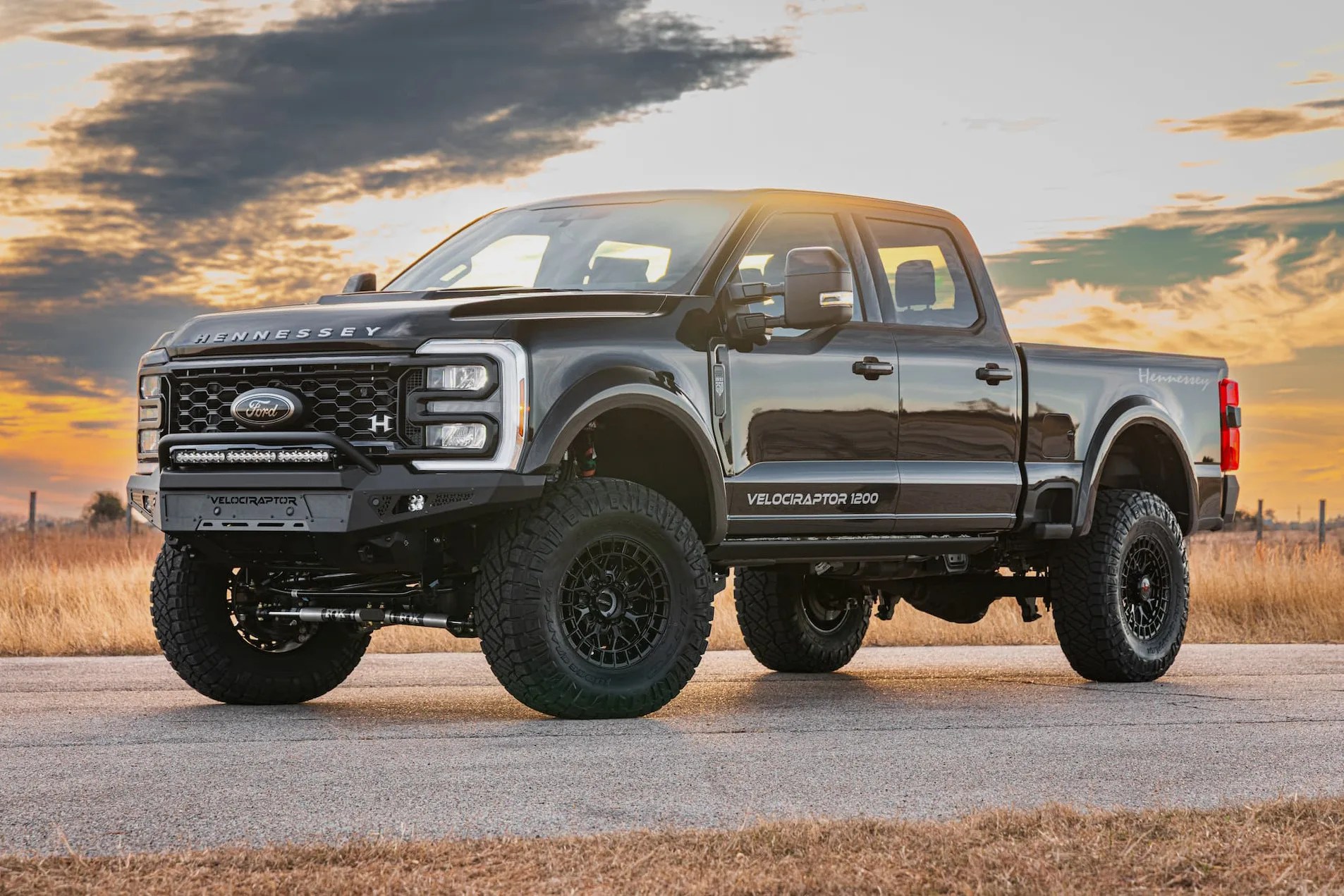 Black Hennessey VelociRaptor 1200 pickup truck with large off-road tires parked on a road at sunset.