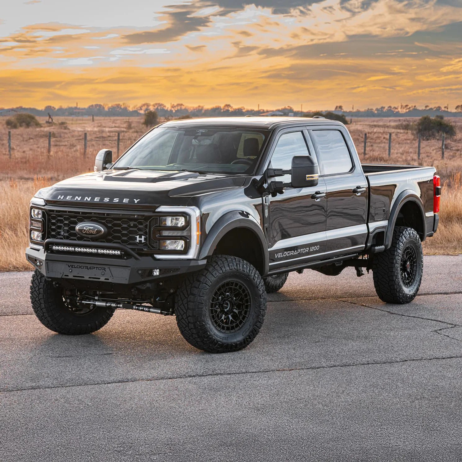 Black Hennessey VelociRaptor 1200 pickup truck with off-road tires parked on a paved road at sunset.