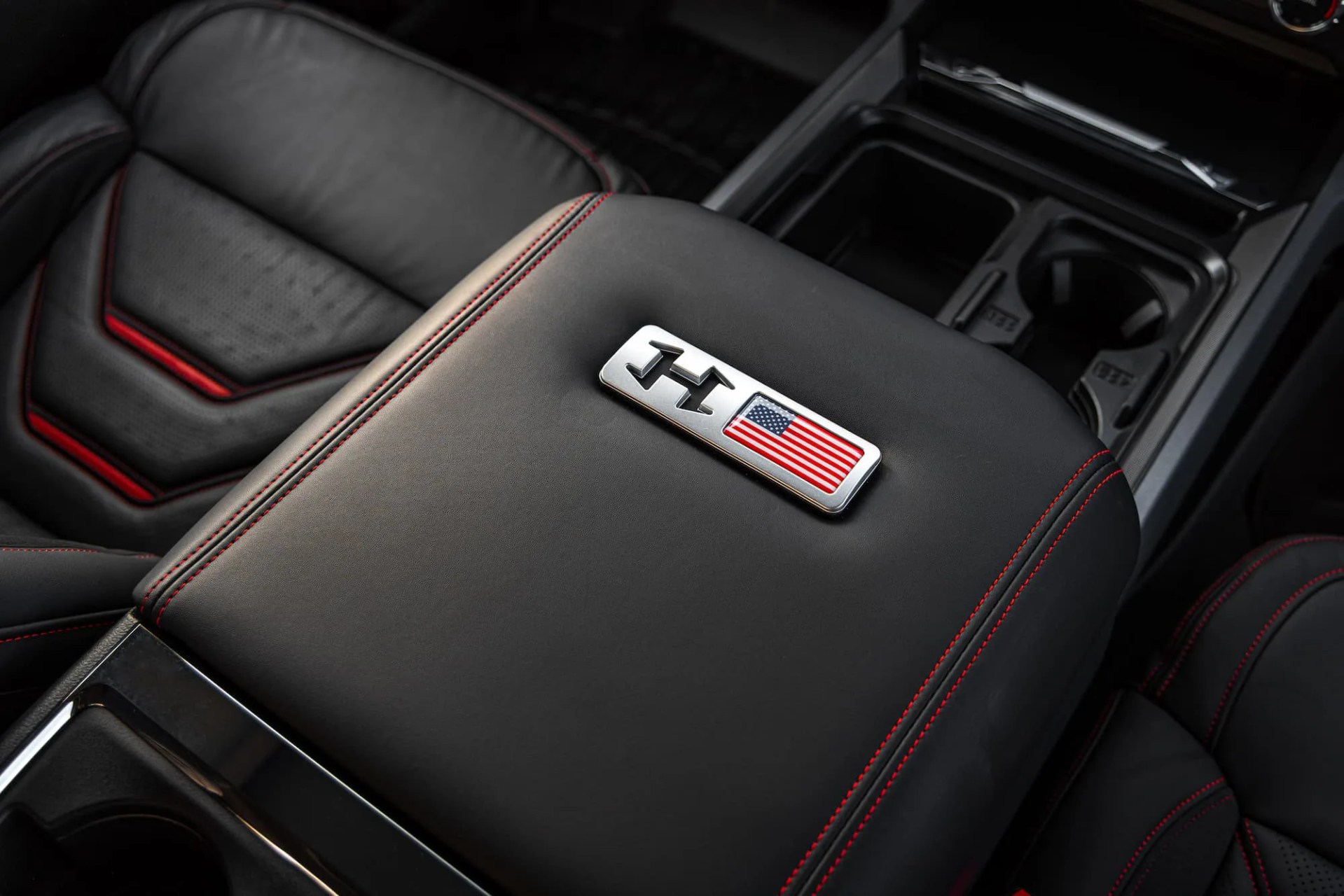 Black leather car armrest with red stitching and a metal emblem featuring an "H" and an American flag.