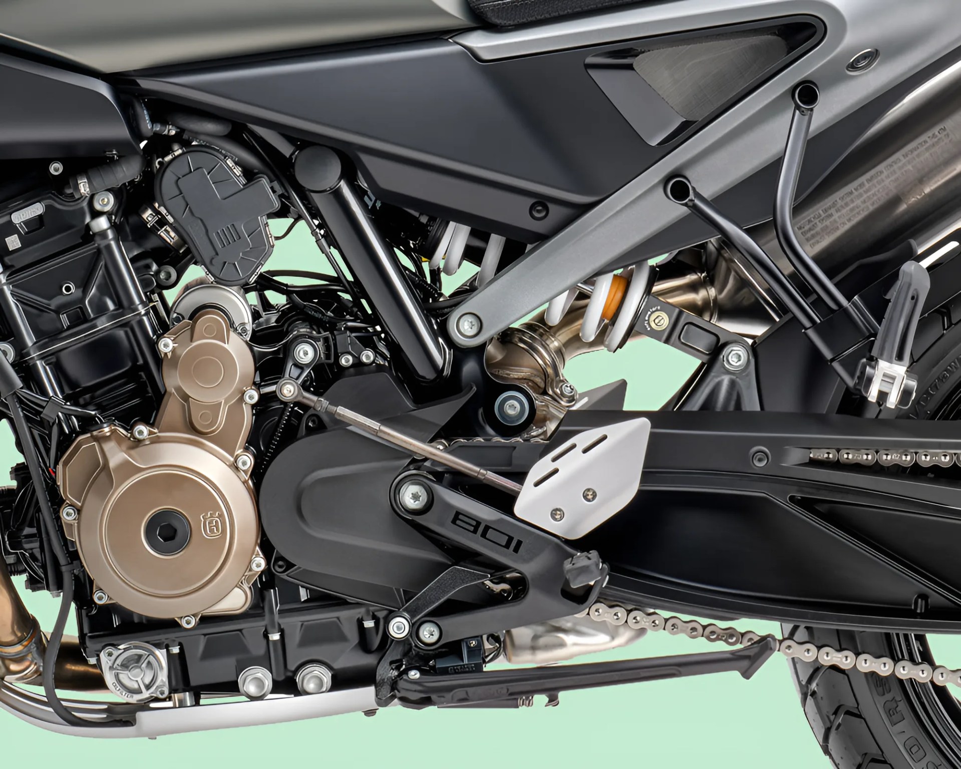Close-up of a motorcycle engine and rear suspension with a gold-colored engine cover and black frame components.