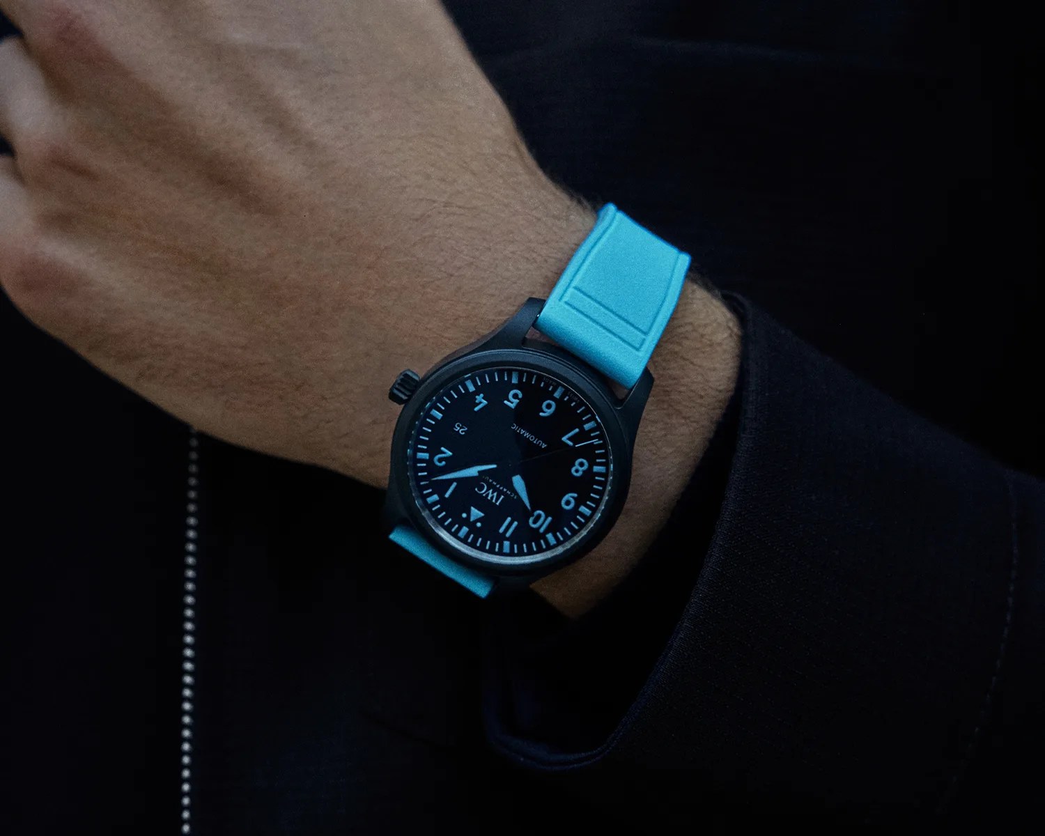Black wristwatch with blue numerals and hands on a wrist with a bright blue strap.