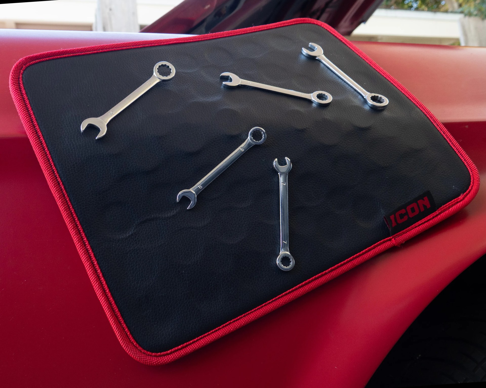 Set of five chrome combination wrenches on a black and red ICON-branded mat on a red surface.