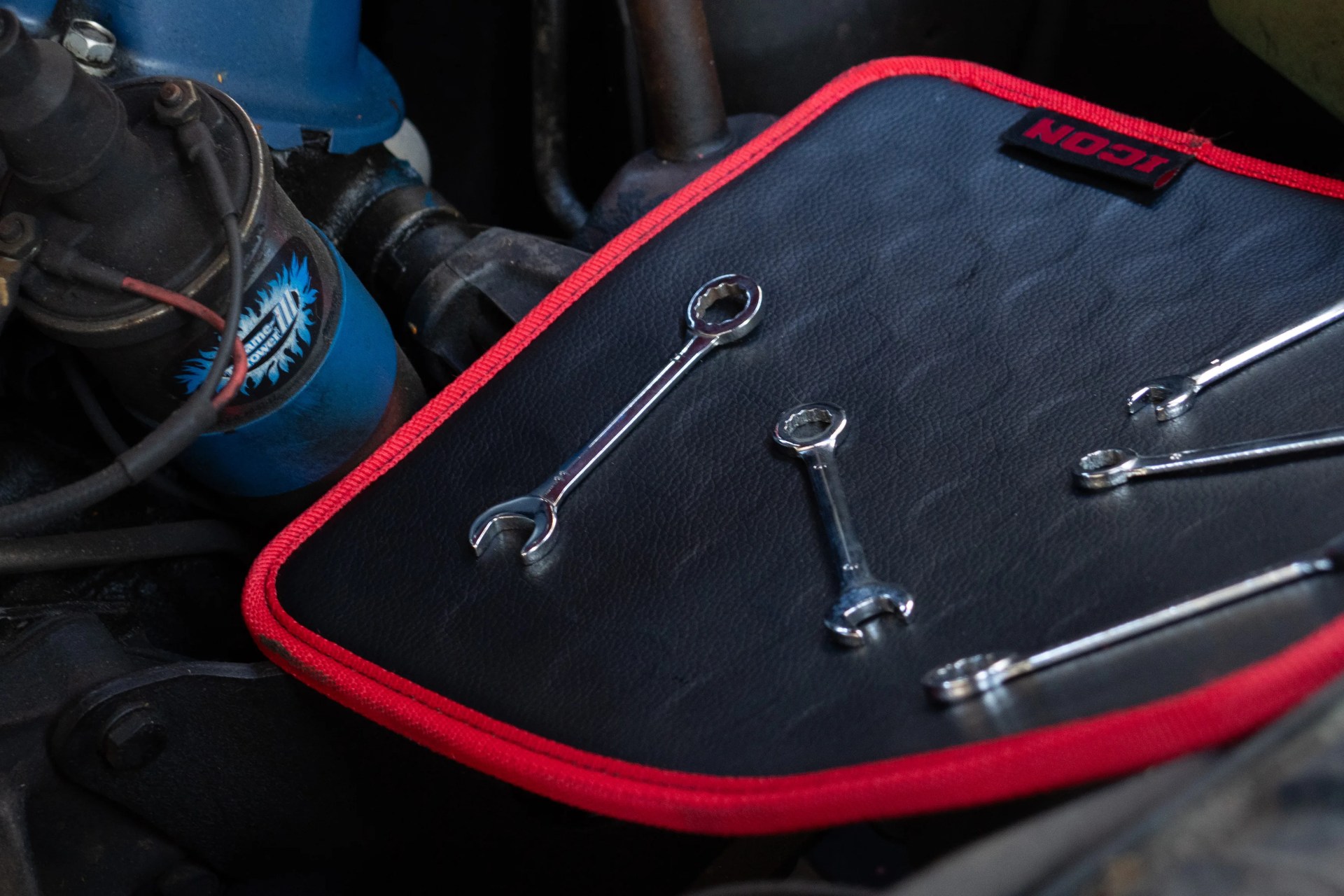 Set of chrome combination wrenches on a black mat with red trim inside a vehicle engine compartment.