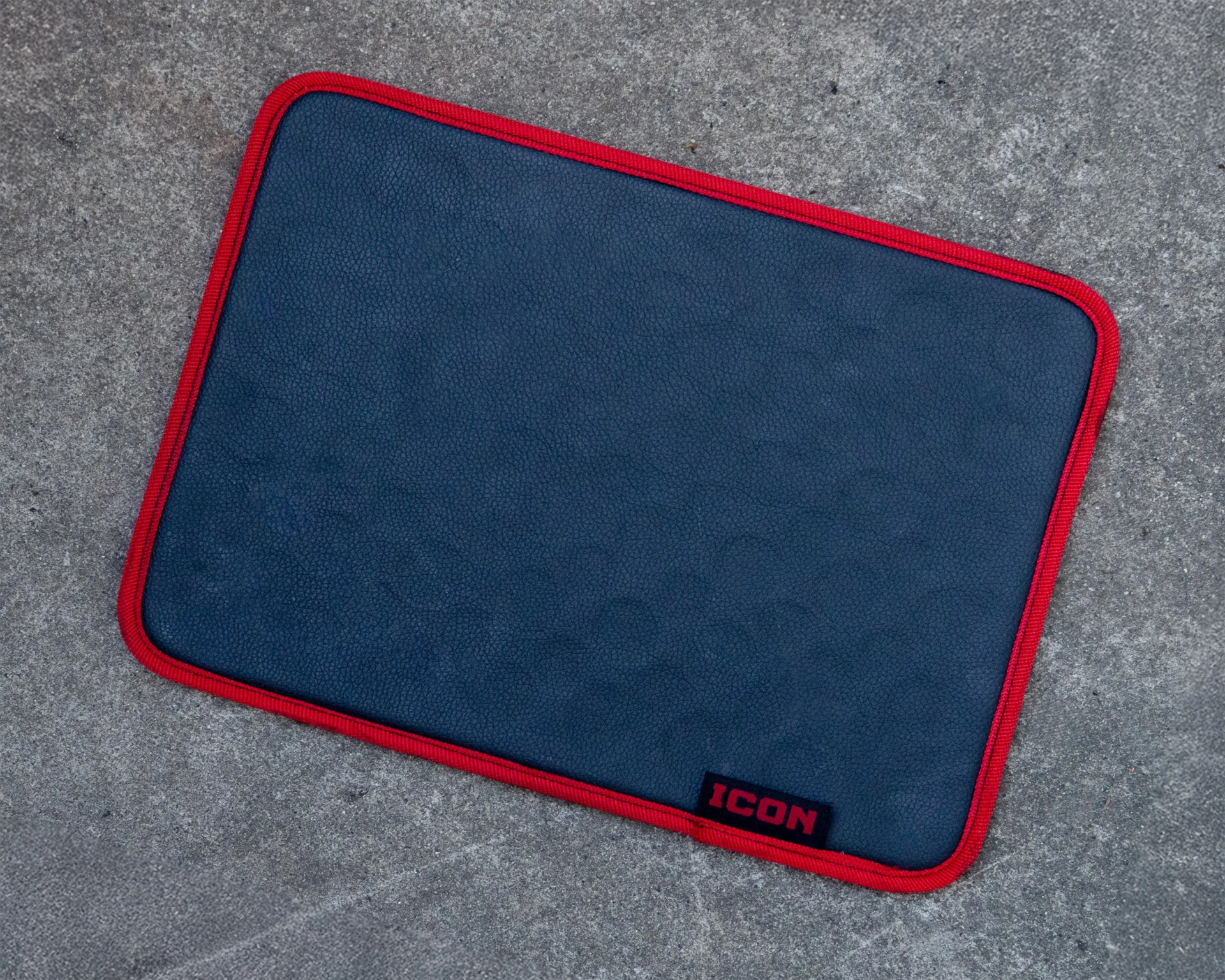 Rectangular dark blue mat with red trim and a black label reading "ICON" on a concrete surface.