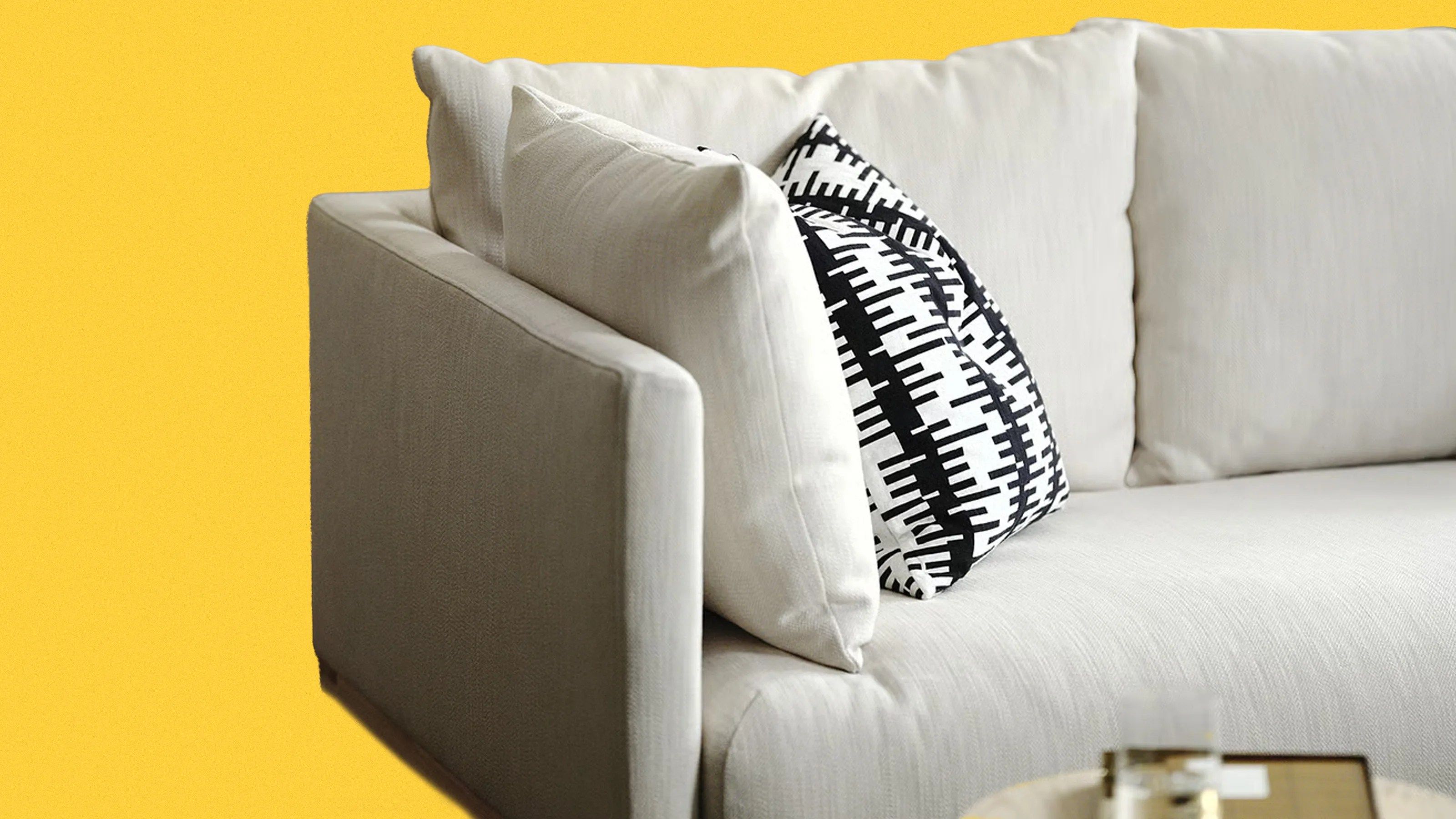 Light beige fabric sofa with white and black patterned throw pillows against a yellow background.
