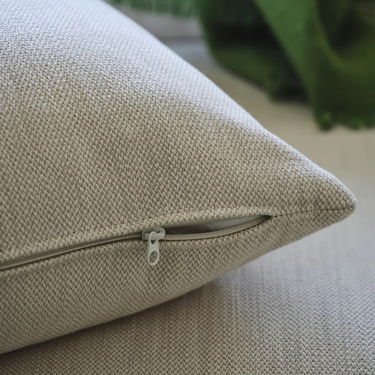 Beige textured fabric pillow with a partially open zipper on a matching surface.