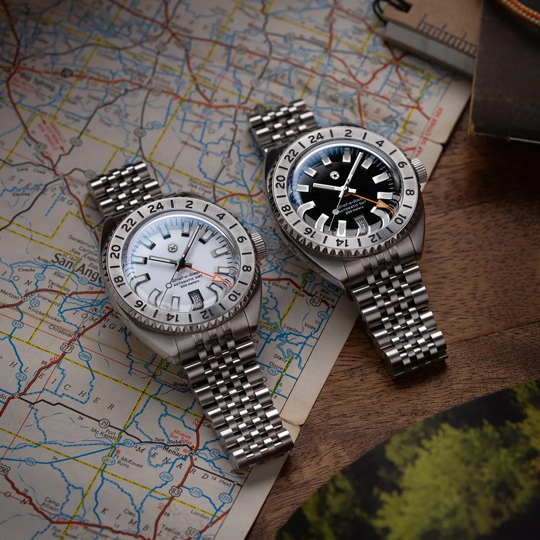 Two stainless steel wristwatches with black and white dials and 24-hour bezels on a map and wooden surface.