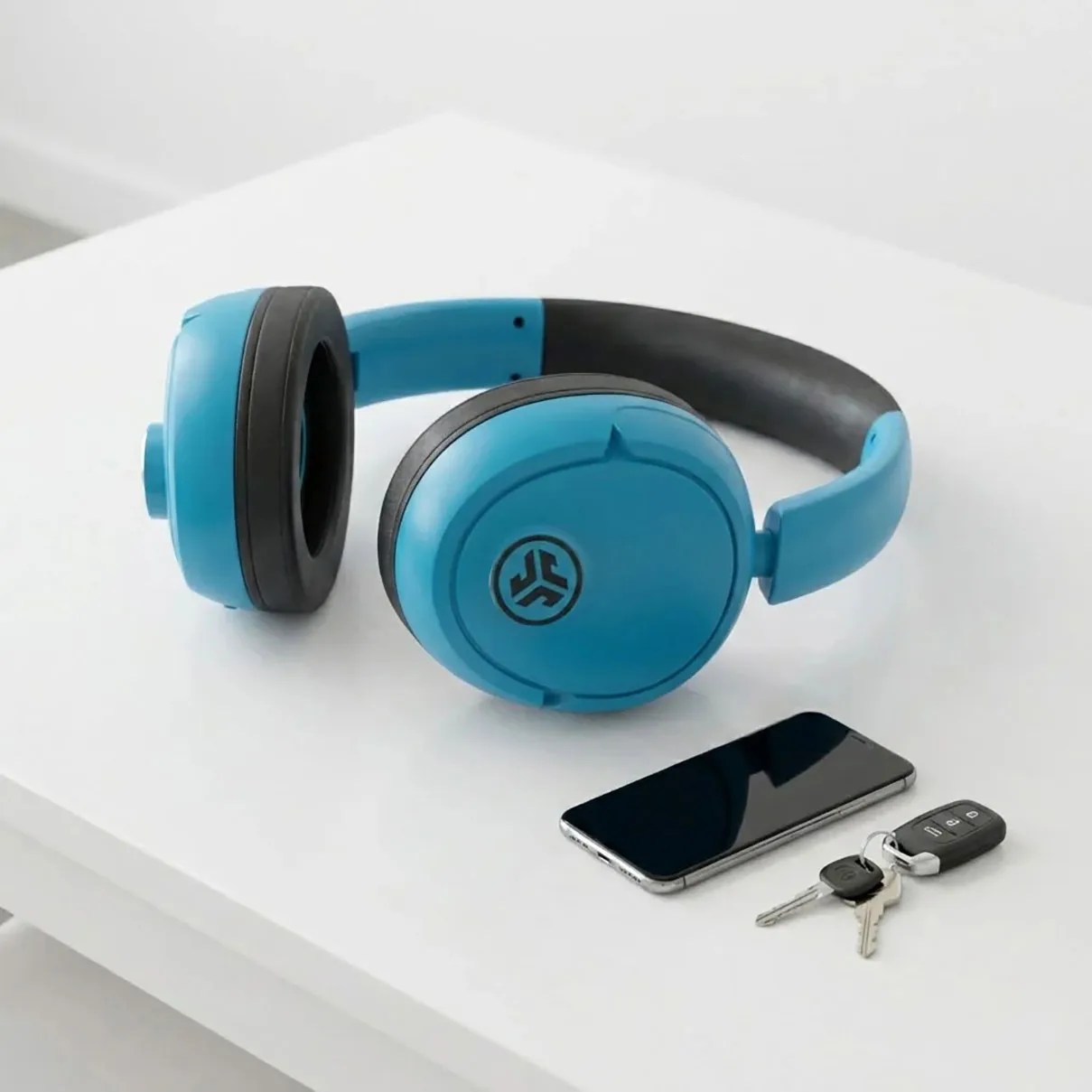Blue over-ear wireless headphones with black ear cushions placed on a white table next to a smartphone and car keys.