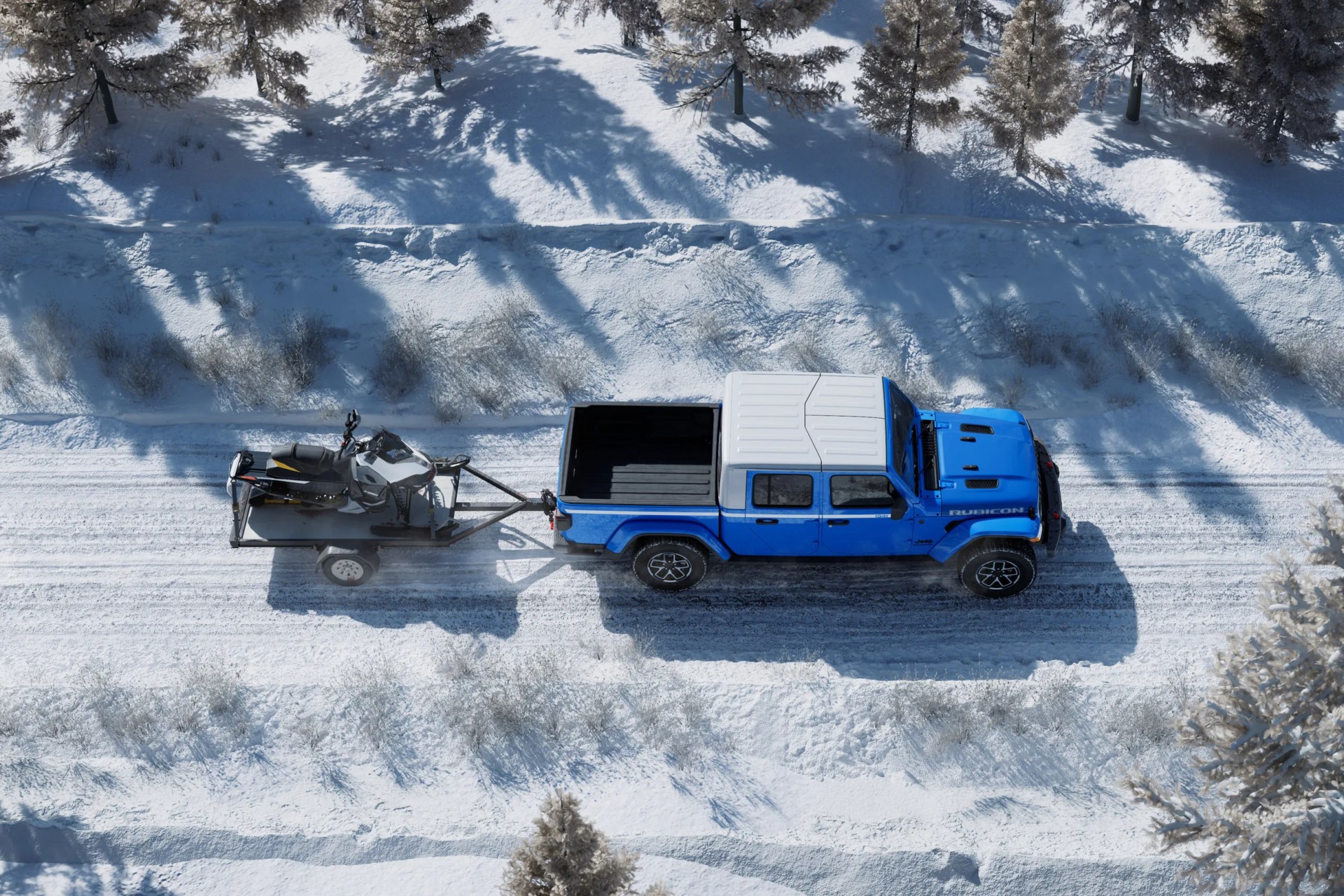 Blue Jeep Gladiator Rubicon towing a trailer with a snowmobile on a snowy road surrounded by trees.