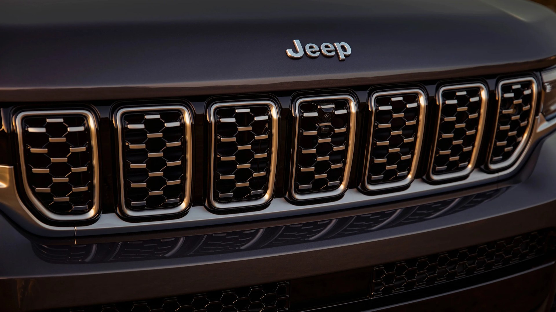 Close-up of a black Jeep front grille with seven vertical slots and the Jeep logo above.