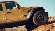 Yellow Jeep Wrangler Willys climbing rocky terrain with visible rugged tires and black fender flares.