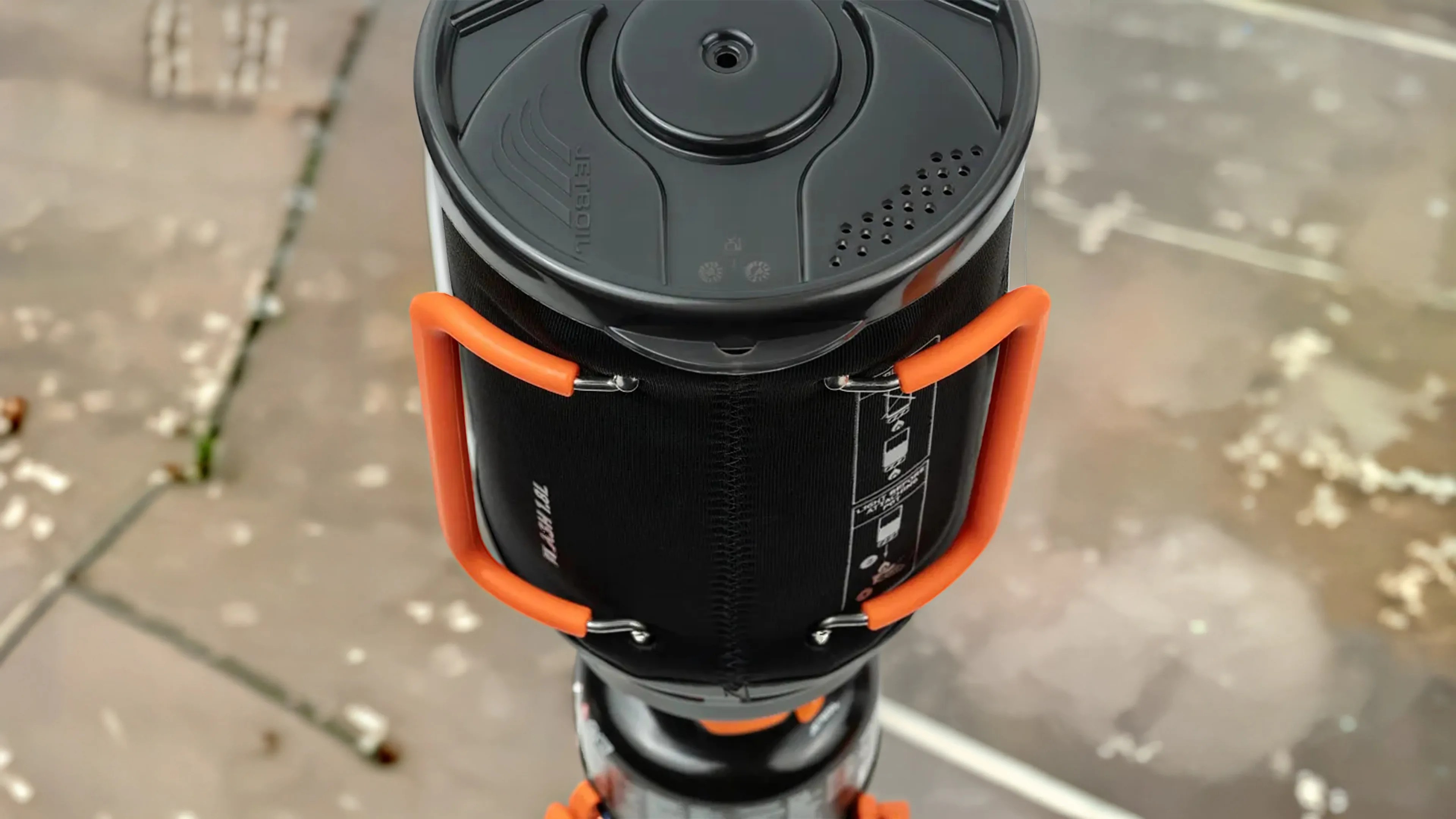 Top view of a black camping stove with orange handles on a stone surface.