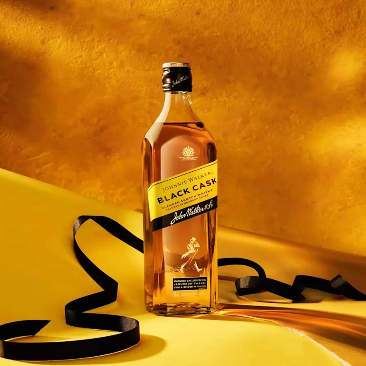 Bottle of Johnnie Walker Black Cask blended Scotch whisky with a black ribbon on a yellow surface.