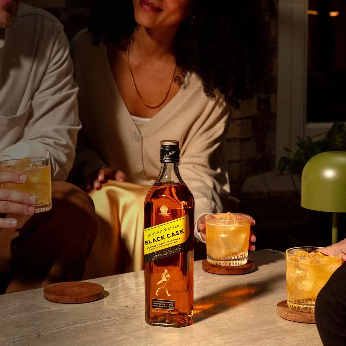 Bottle of Johnnie Walker Black Cask whisky on a table with three glasses of whisky and ice.