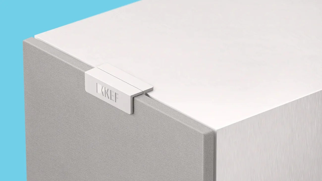 White and gray KEF speaker with fabric front and white top against a blue background.