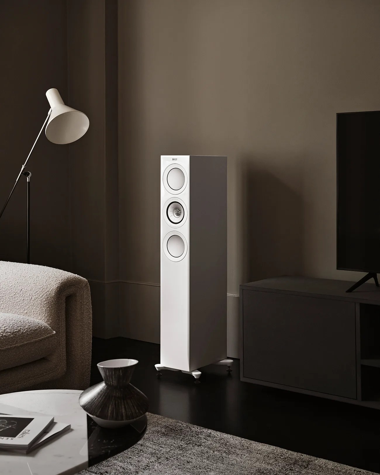 White floor-standing speaker with three circular drivers in a modern living room setting.