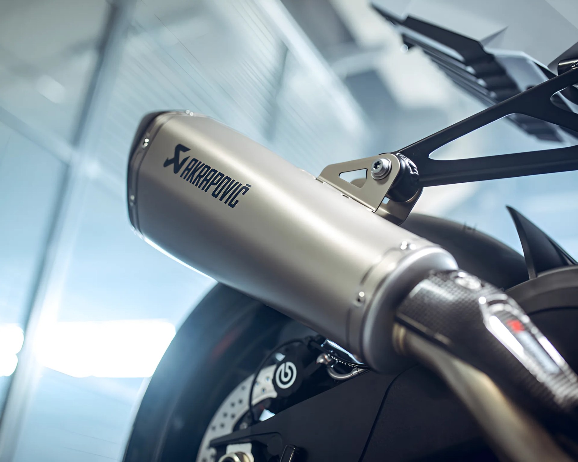 Silver Akrapovič motorcycle exhaust with carbon fiber tip mounted on a black motorcycle.