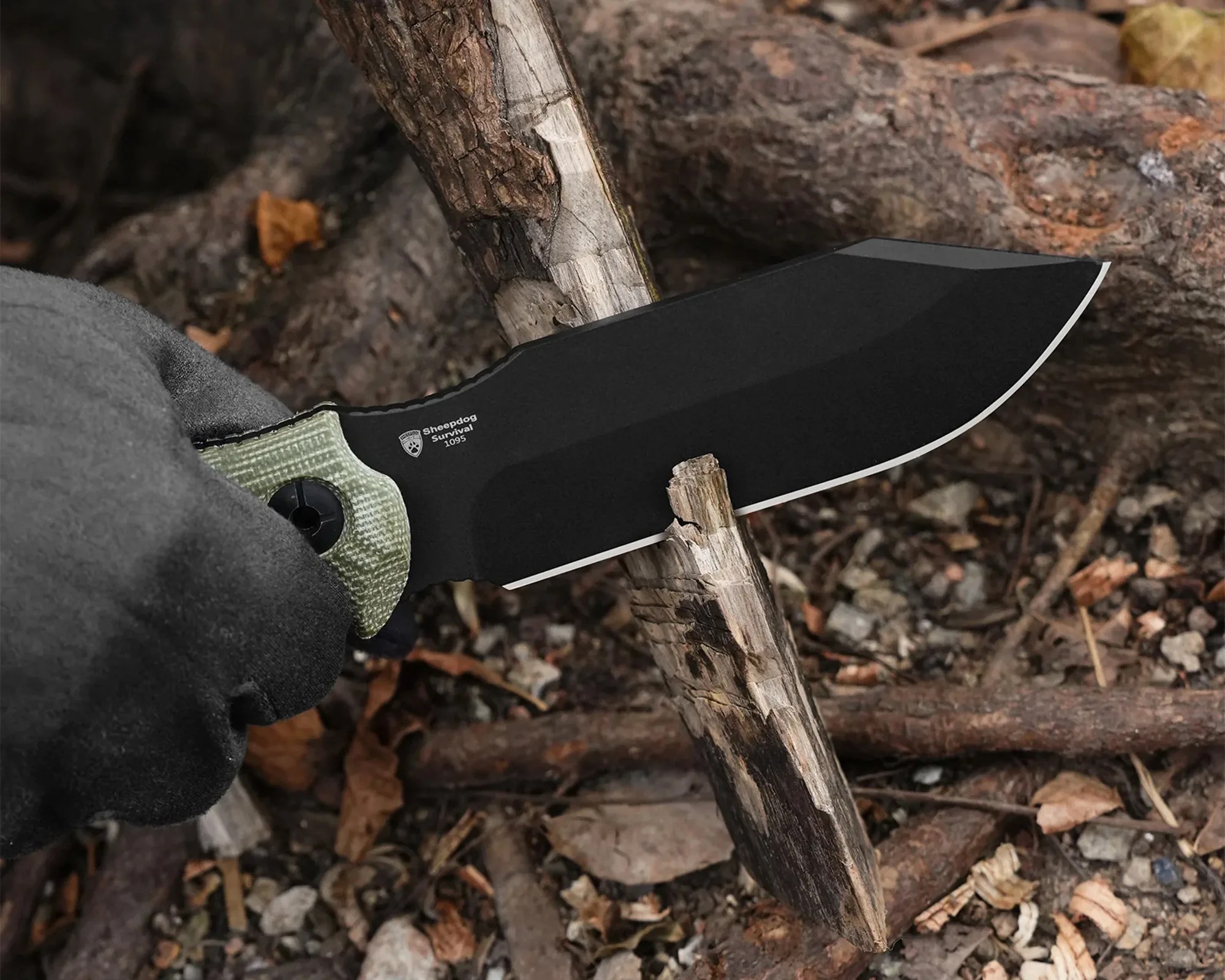 Black fixed-blade knife with green handle cutting a small branch held by a gloved hand.