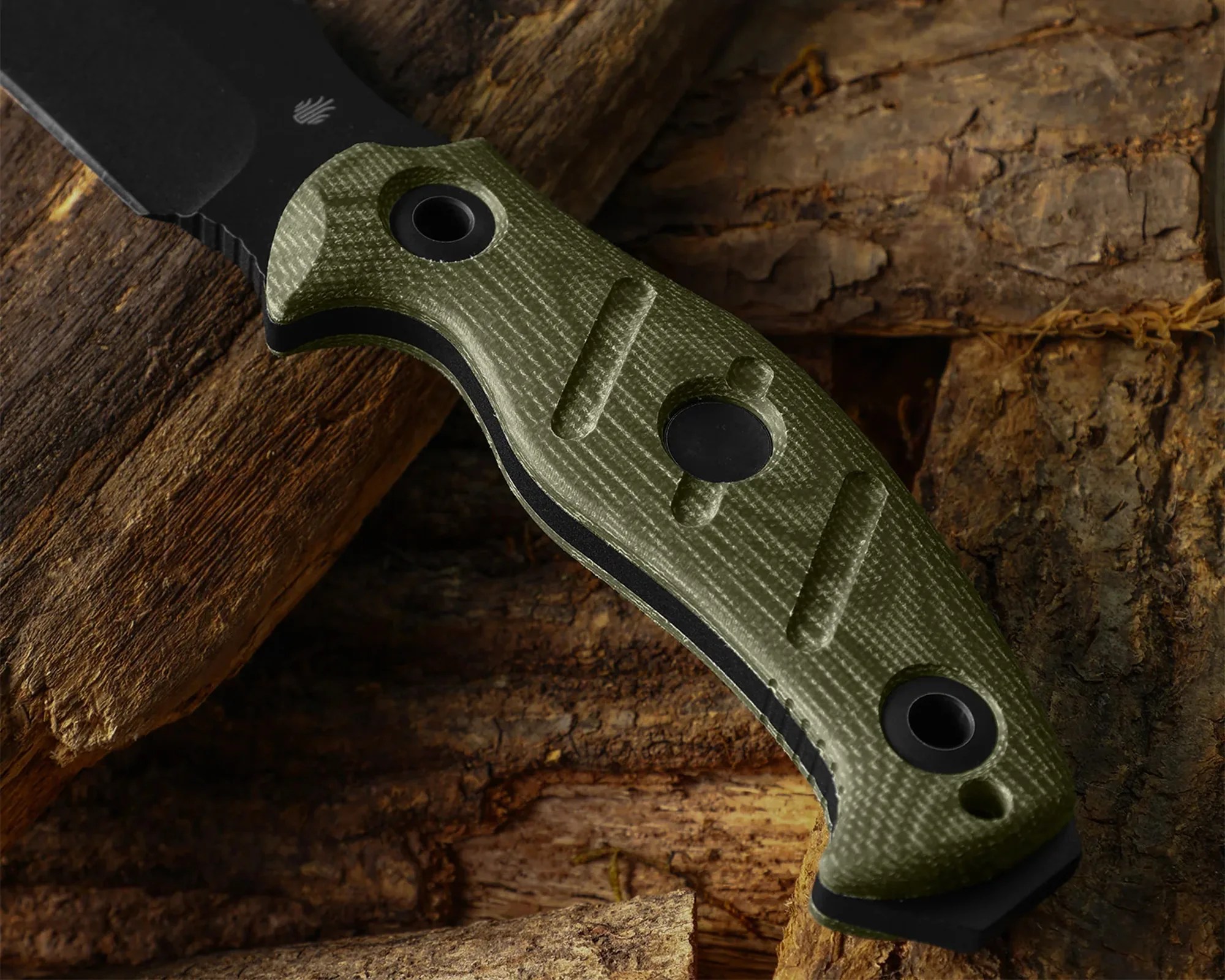 Close-up of a green textured knife handle with black rivets resting on rough wooden logs.