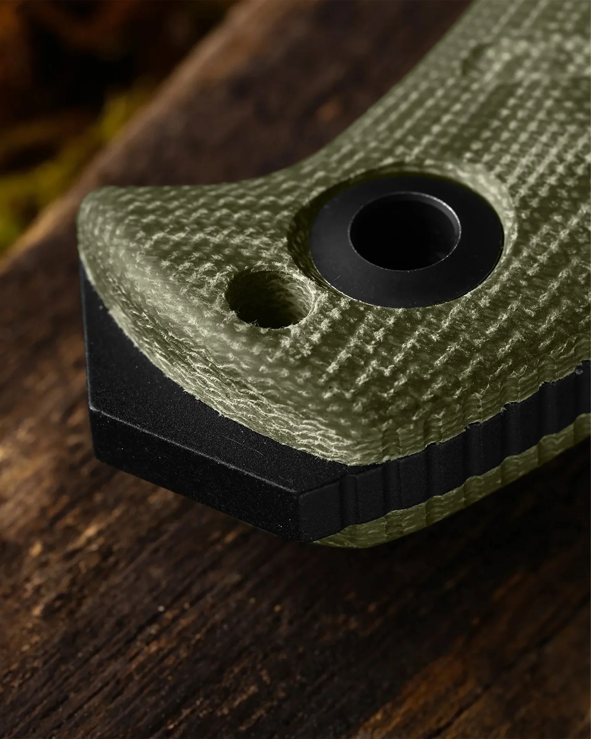 Close-up of a textured olive green handle with a black metal base and circular hole on a wooden surface.