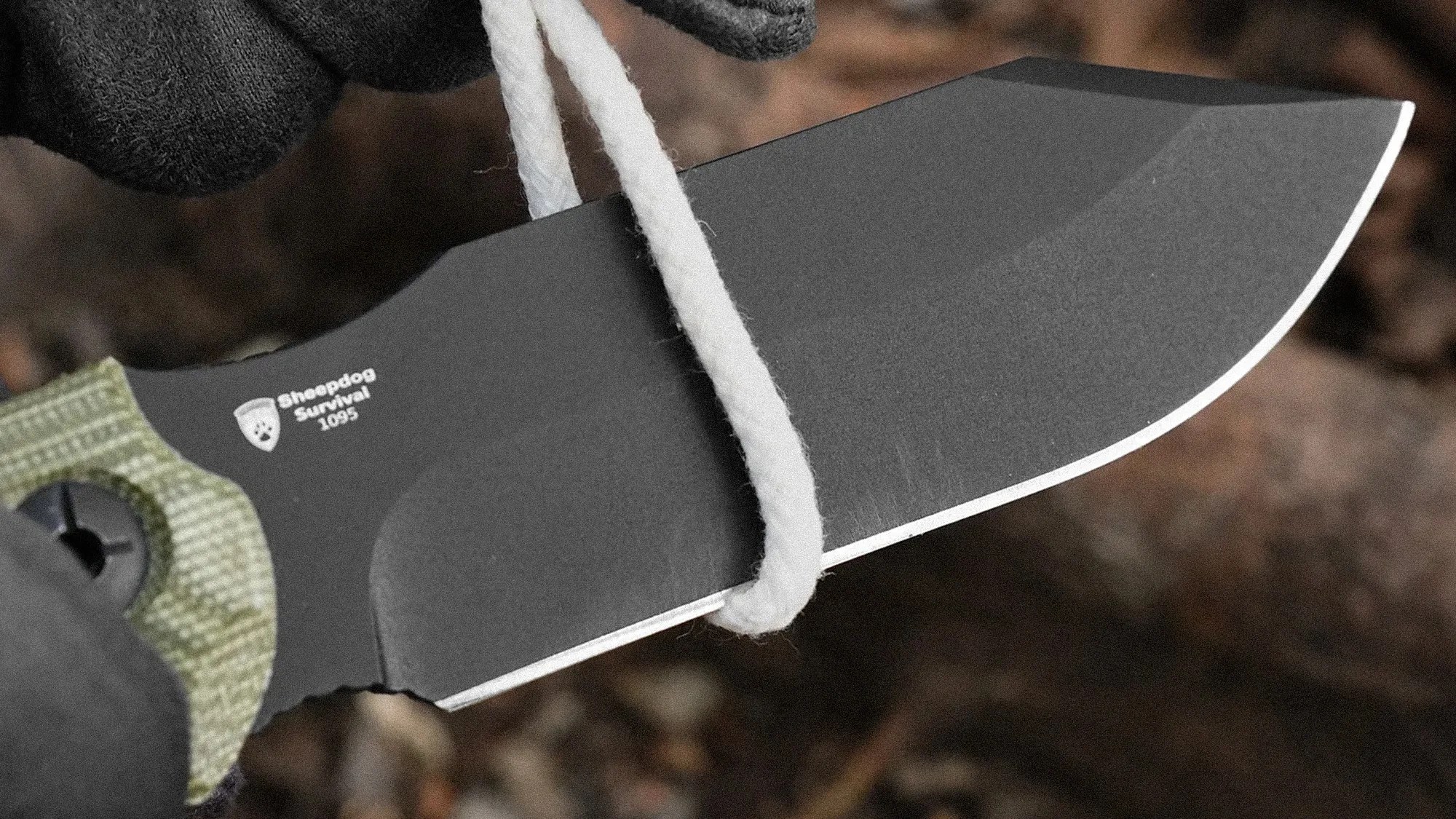 Black Sheepdog Survival 1095 fixed blade knife with green textured handle cutting white rope.