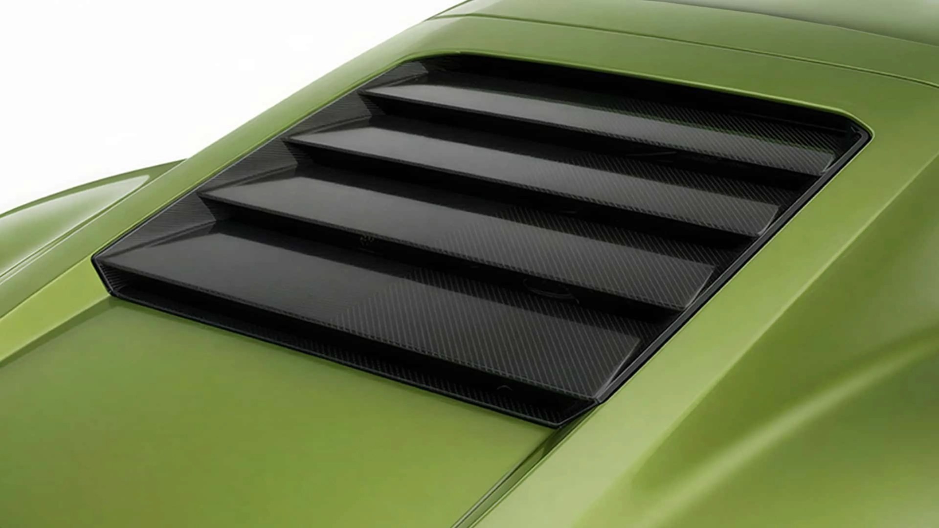 Close-up of black carbon fiber rear window louvers on a green car hood.