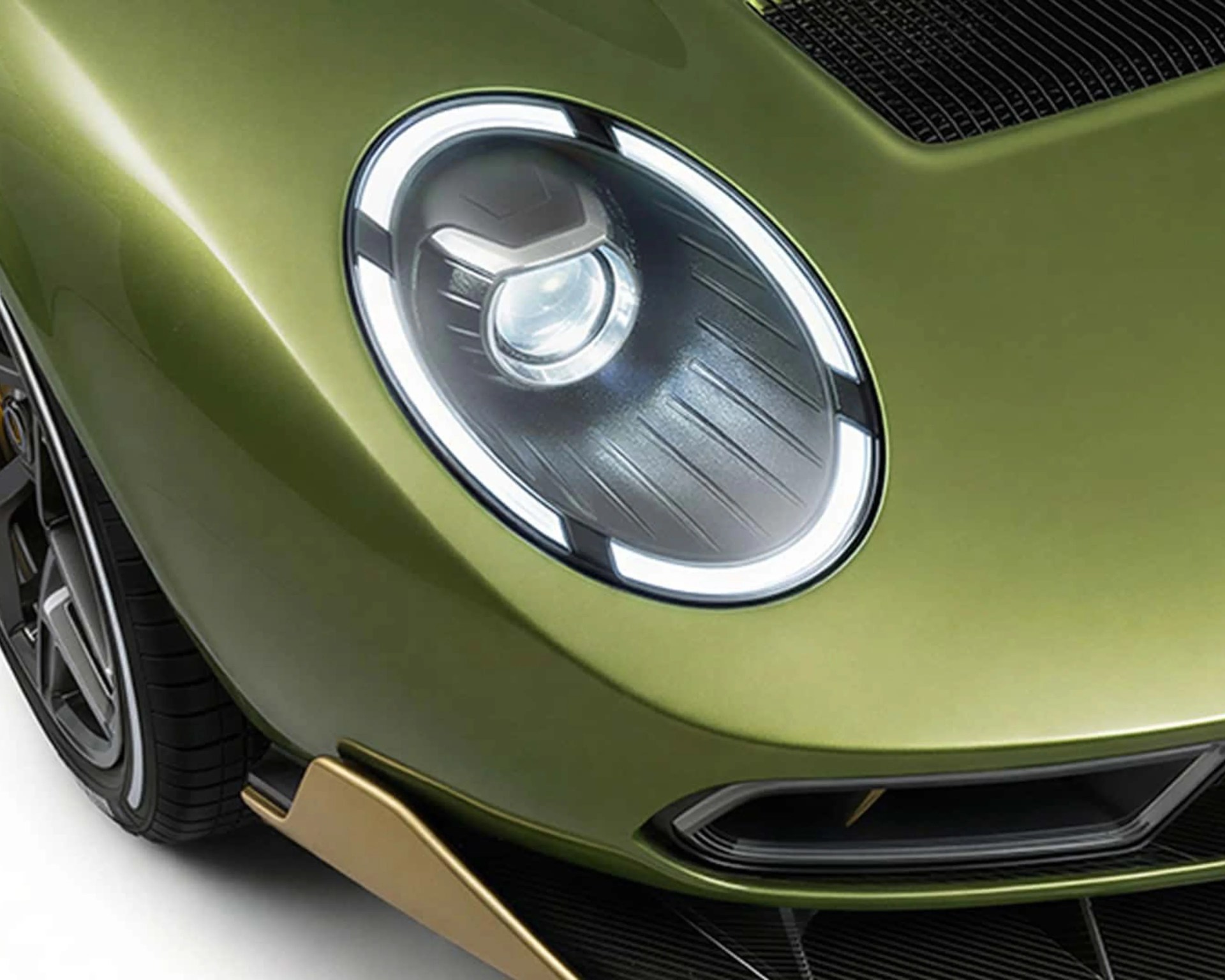 Close-up of a round LED headlight on a metallic olive green sports car with a gold side skirt.