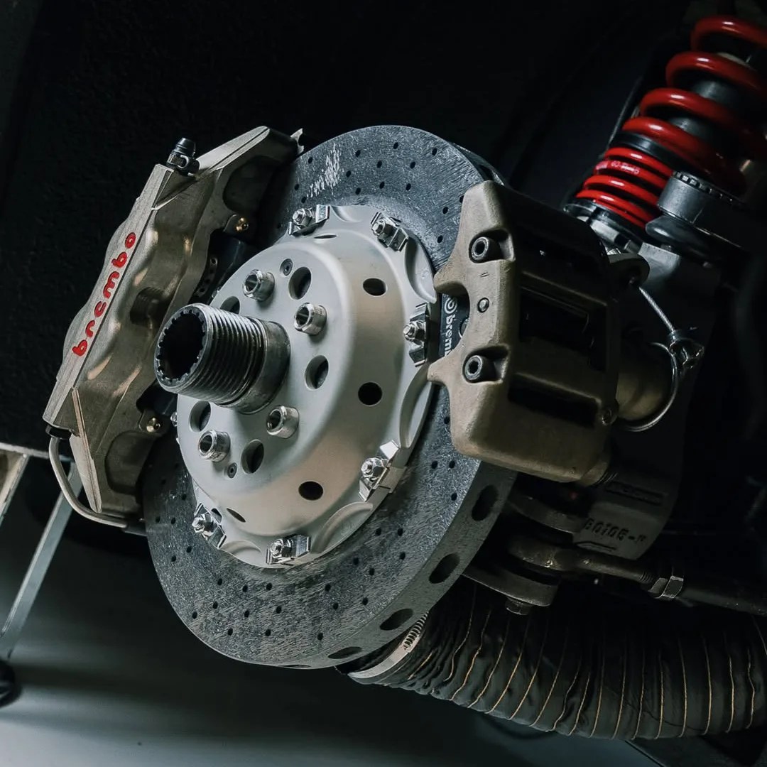 Close-up of a Brembo brake caliper and drilled brake disc with a red coil spring in the background.