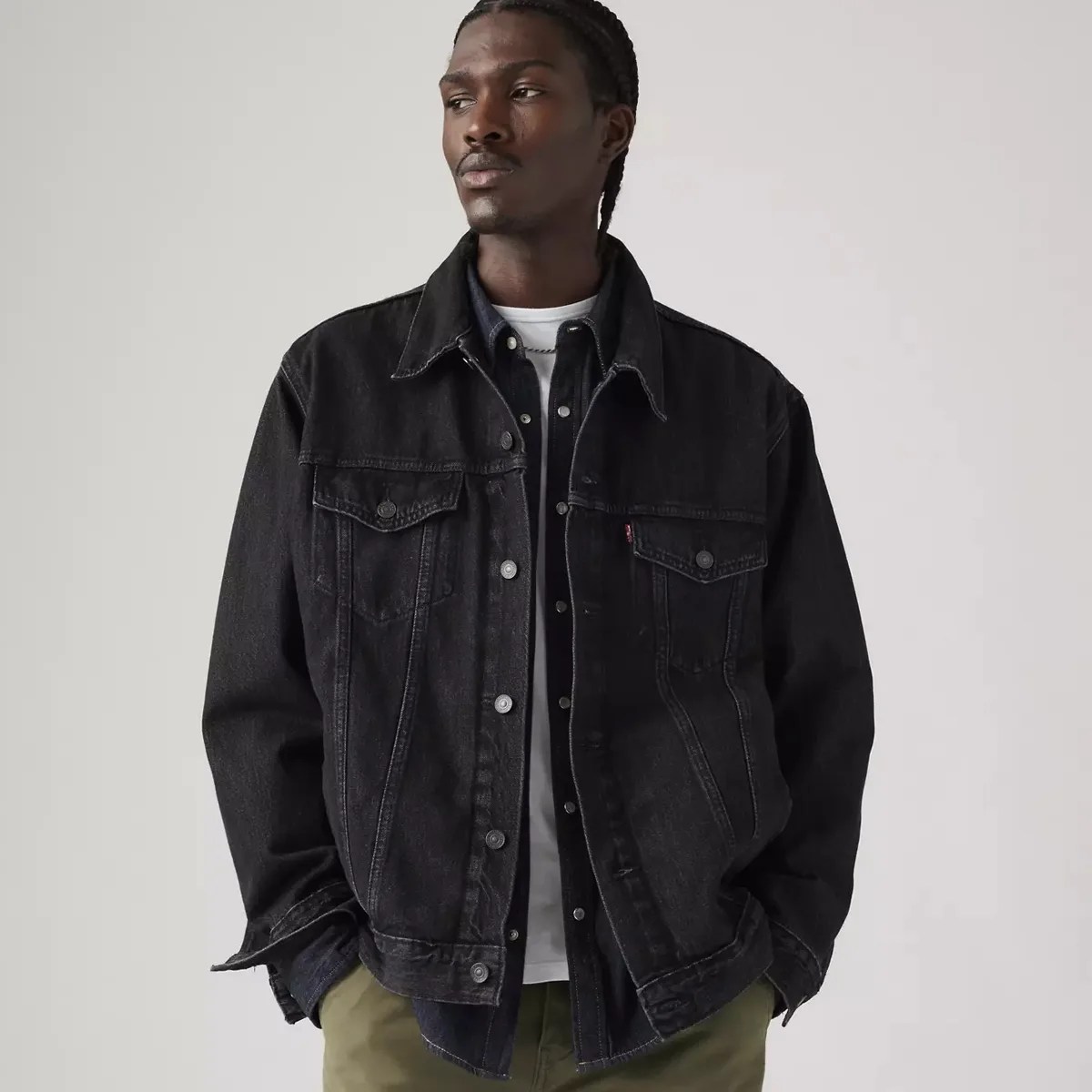 Black denim jacket with button closures and flap chest pockets worn over a dark shirt and white t-shirt.