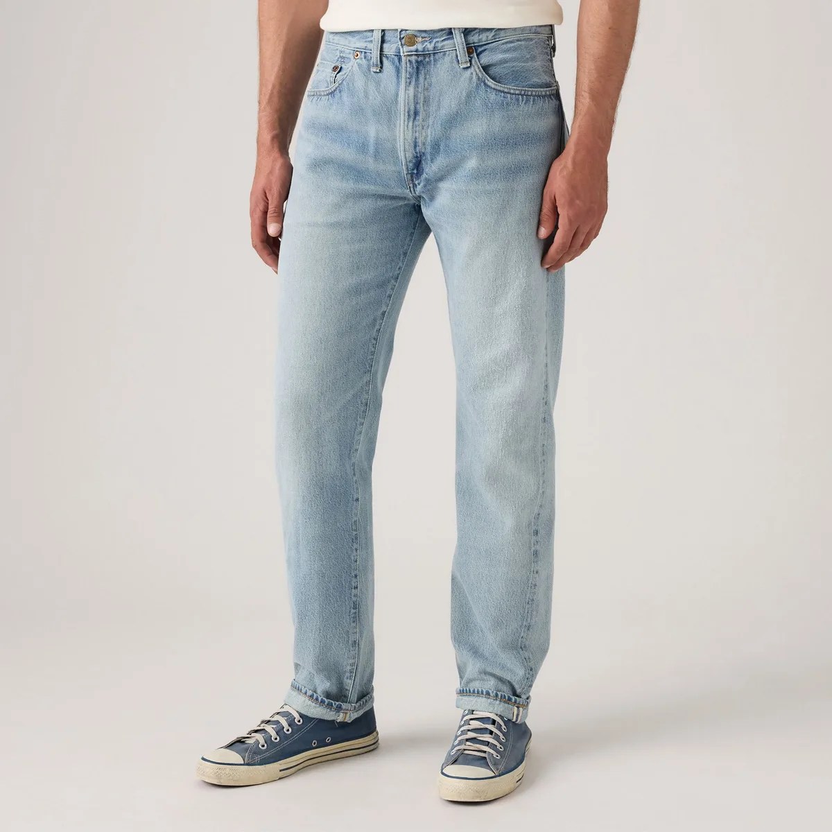 Light blue straight-leg jeans worn with rolled cuffs and navy blue canvas sneakers.