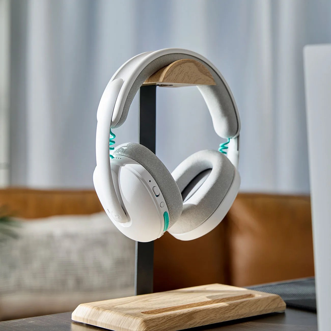 White over-ear headphones with gray ear cushions and teal accents on a wooden and metal stand.