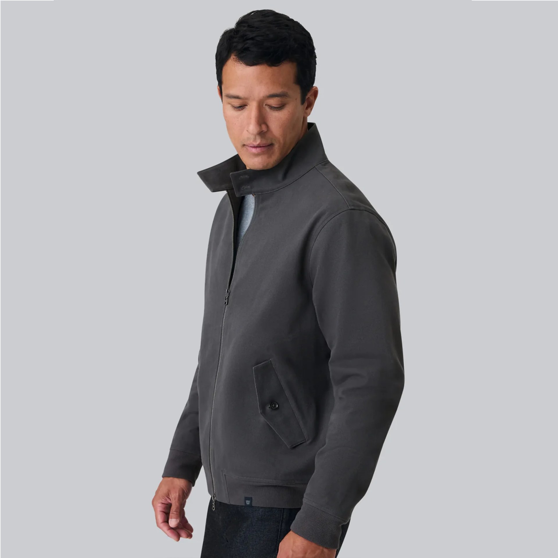 Man wearing a dark gray zip-up jacket with a high collar and buttoned side pockets.