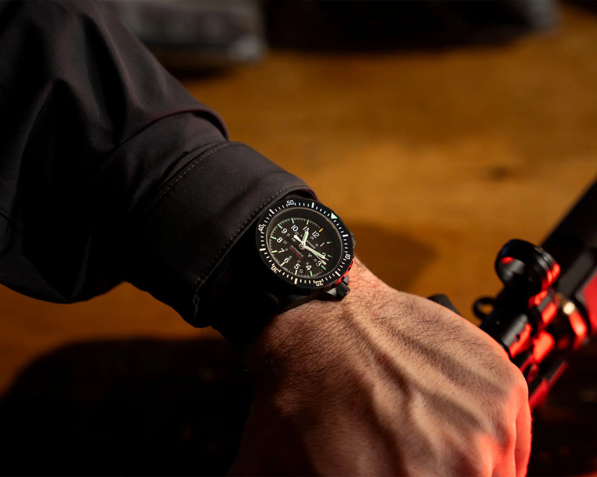 Black wristwatch with a black dial and white numerals worn on a wrist over a black sleeve.