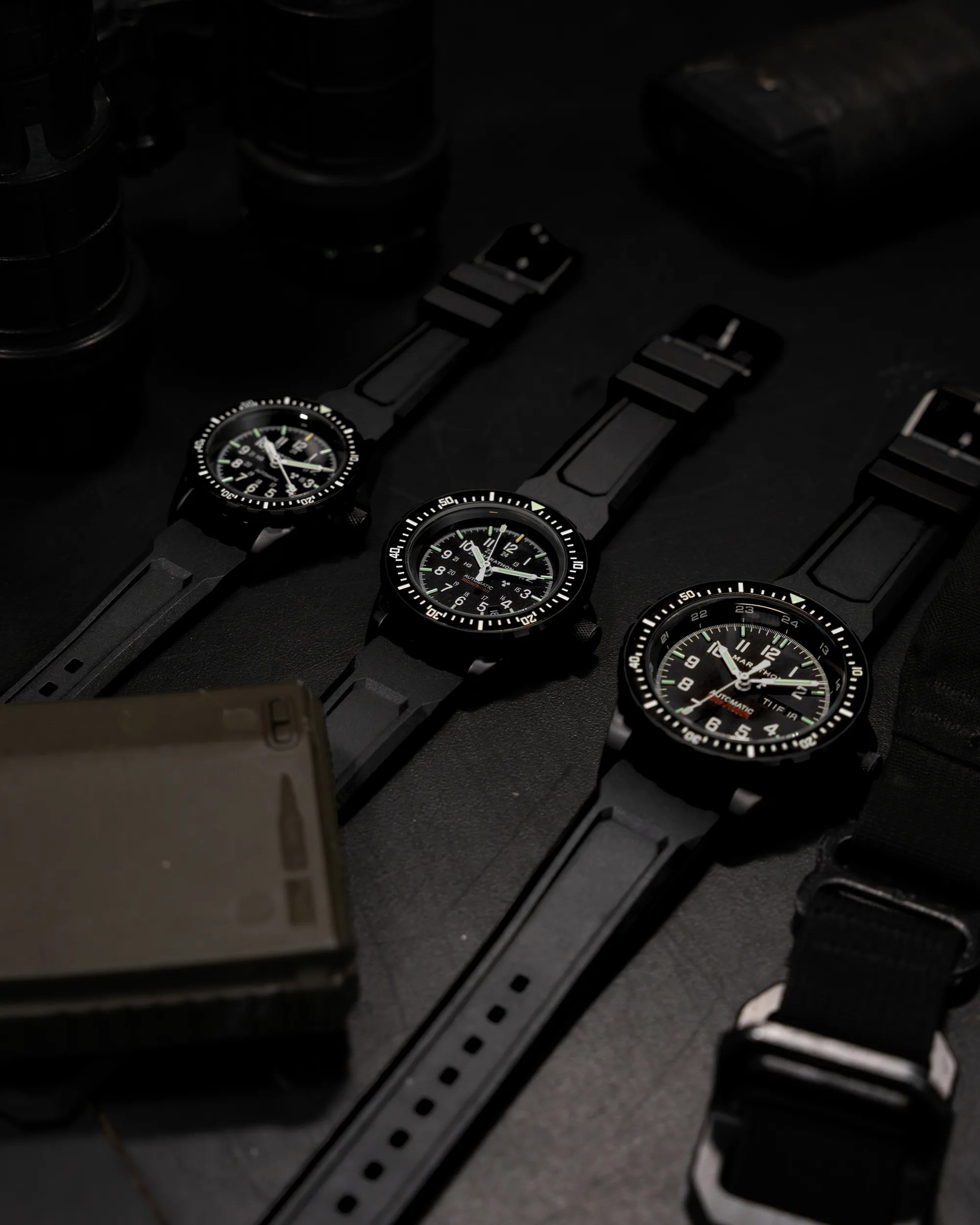 Three black tactical wristwatches with rubber straps arranged diagonally on a dark surface.