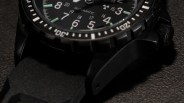 Close-up of a black automatic watch with a textured black strap and white and green markers on the dial.
