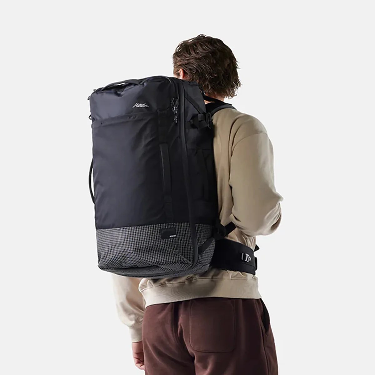 Black and gray large backpack with padded waist belt worn by a person in beige sweatshirt and brown pants.