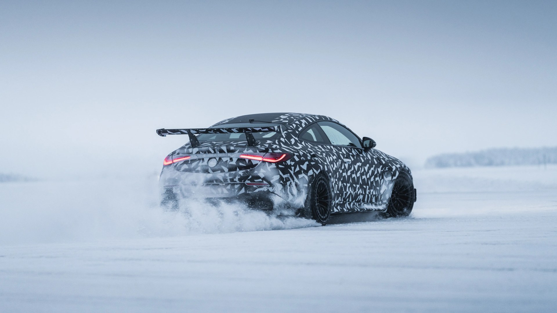 Black and white camouflaged sports car with rear spoiler drifting on snow-covered ground.