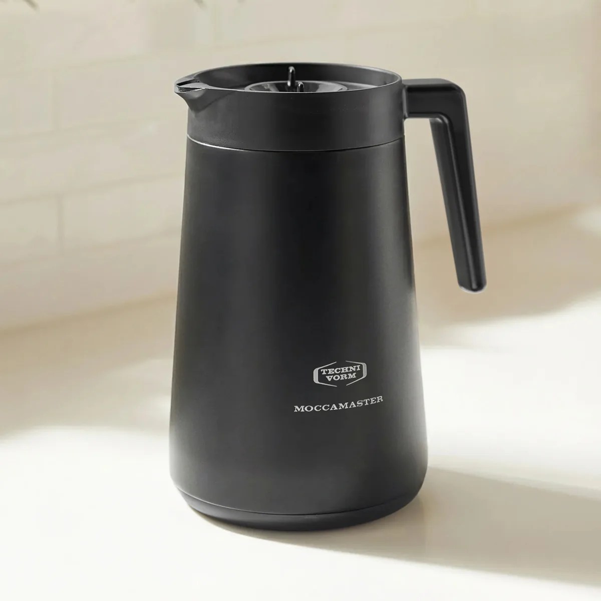 Matte black Moccamaster thermal coffee carafe with handle on a light surface.