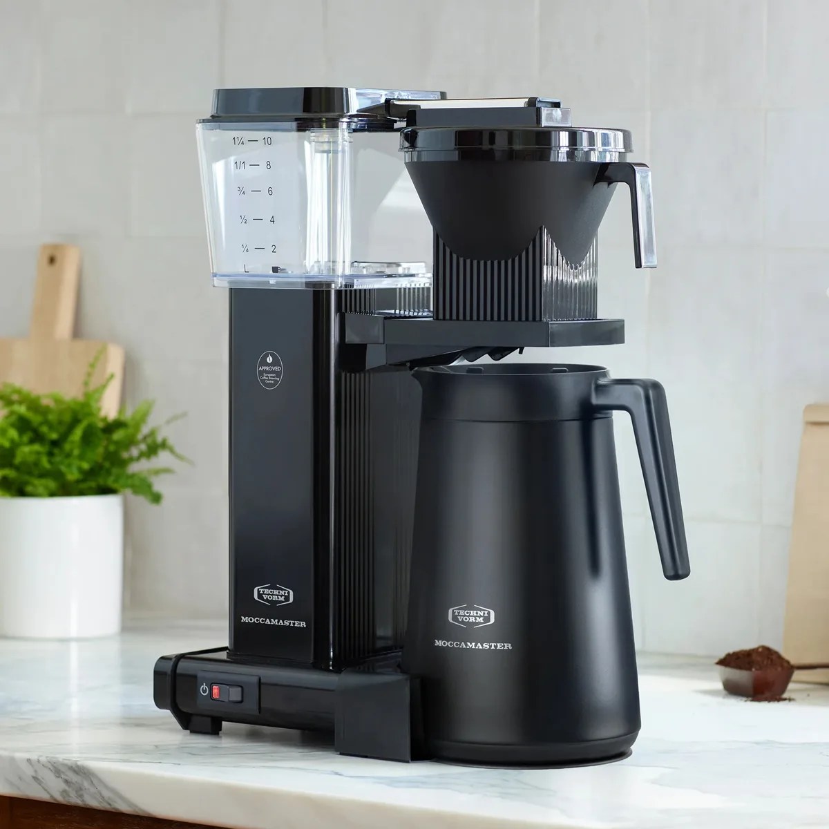 Black Technivorm Moccamaster coffee maker with clear water reservoir on a marble countertop.