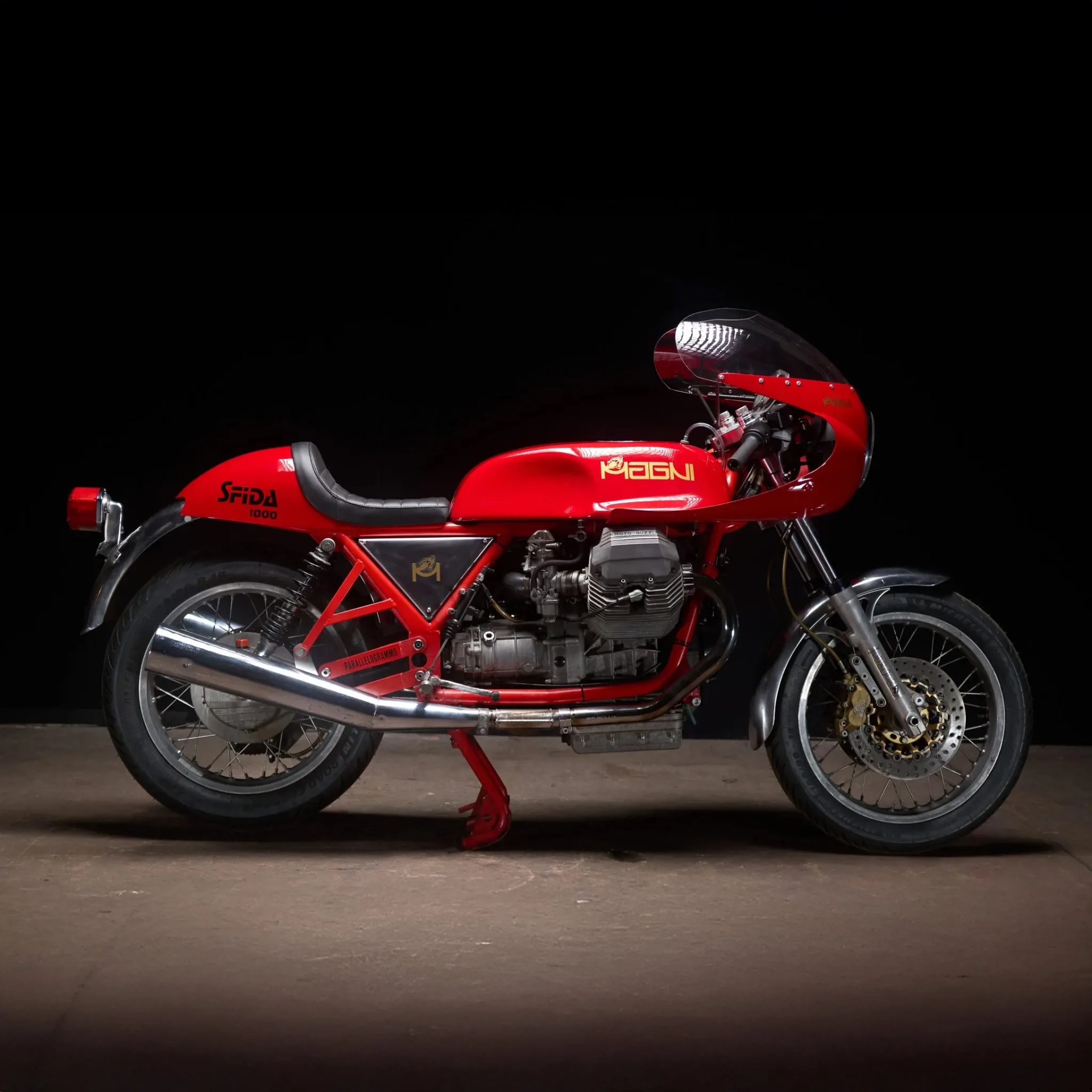 Red Magni Sfida 1000 vintage motorcycle with black seat and chrome exhaust on a dark background.