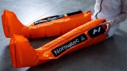 Bright orange Normatec compression leg sleeves worn by a person sitting on a gray floor.