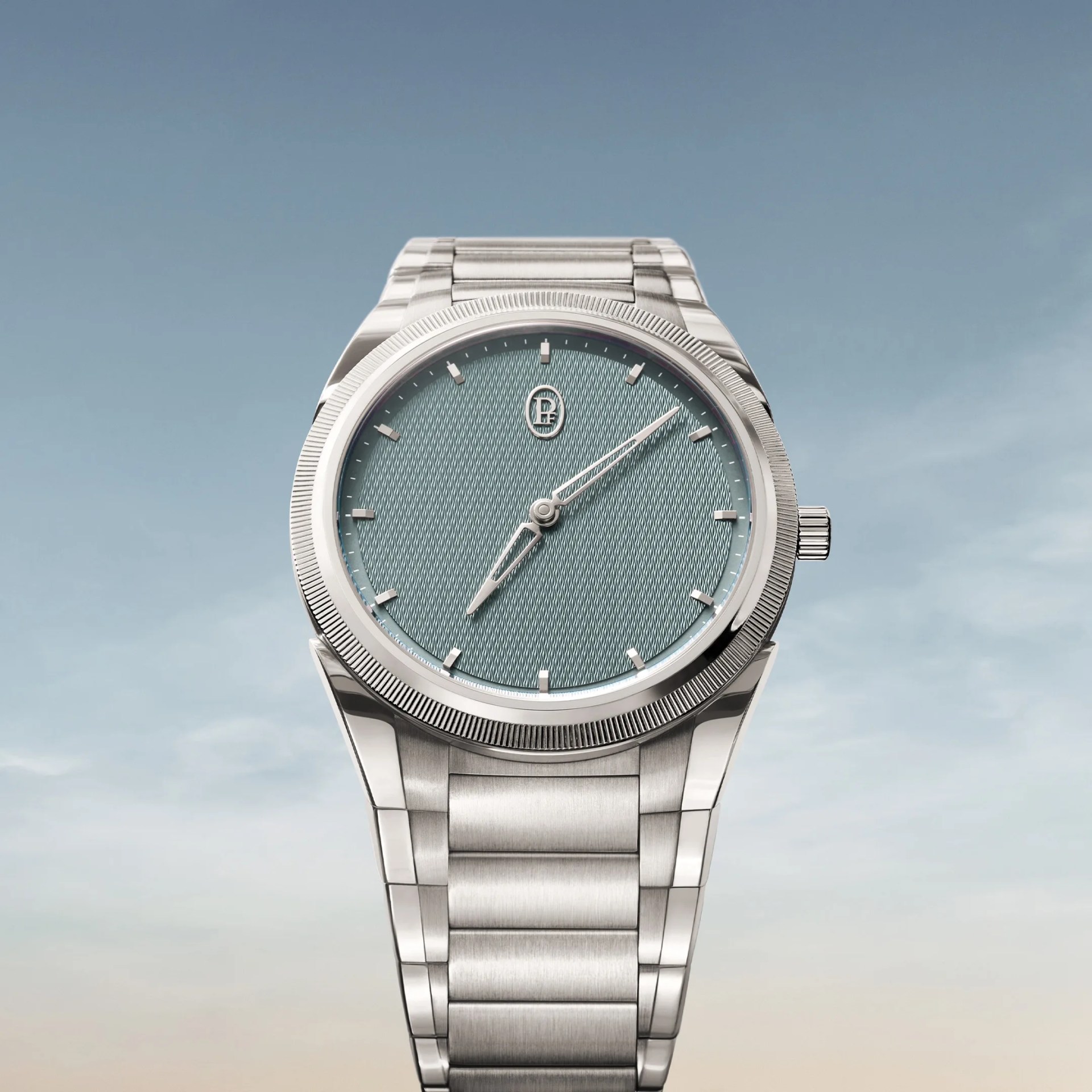 Silver stainless steel wristwatch with textured light blue dial and minimal hour markers against a sky background.