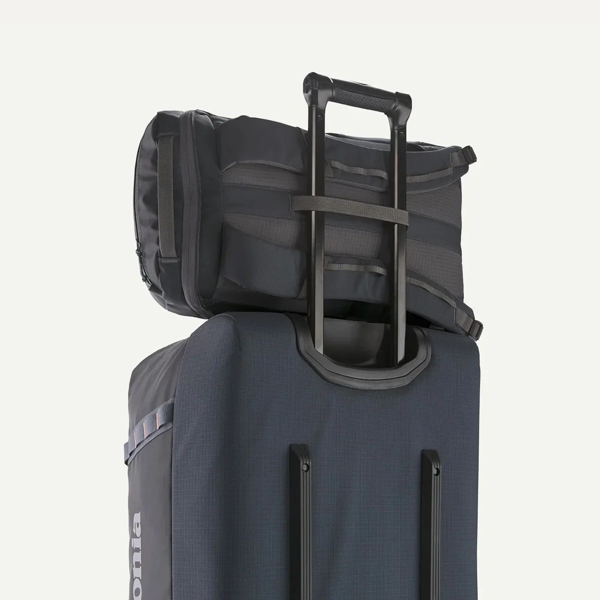 Dark gray backpack secured on the extended handle of a dark blue rolling suitcase.