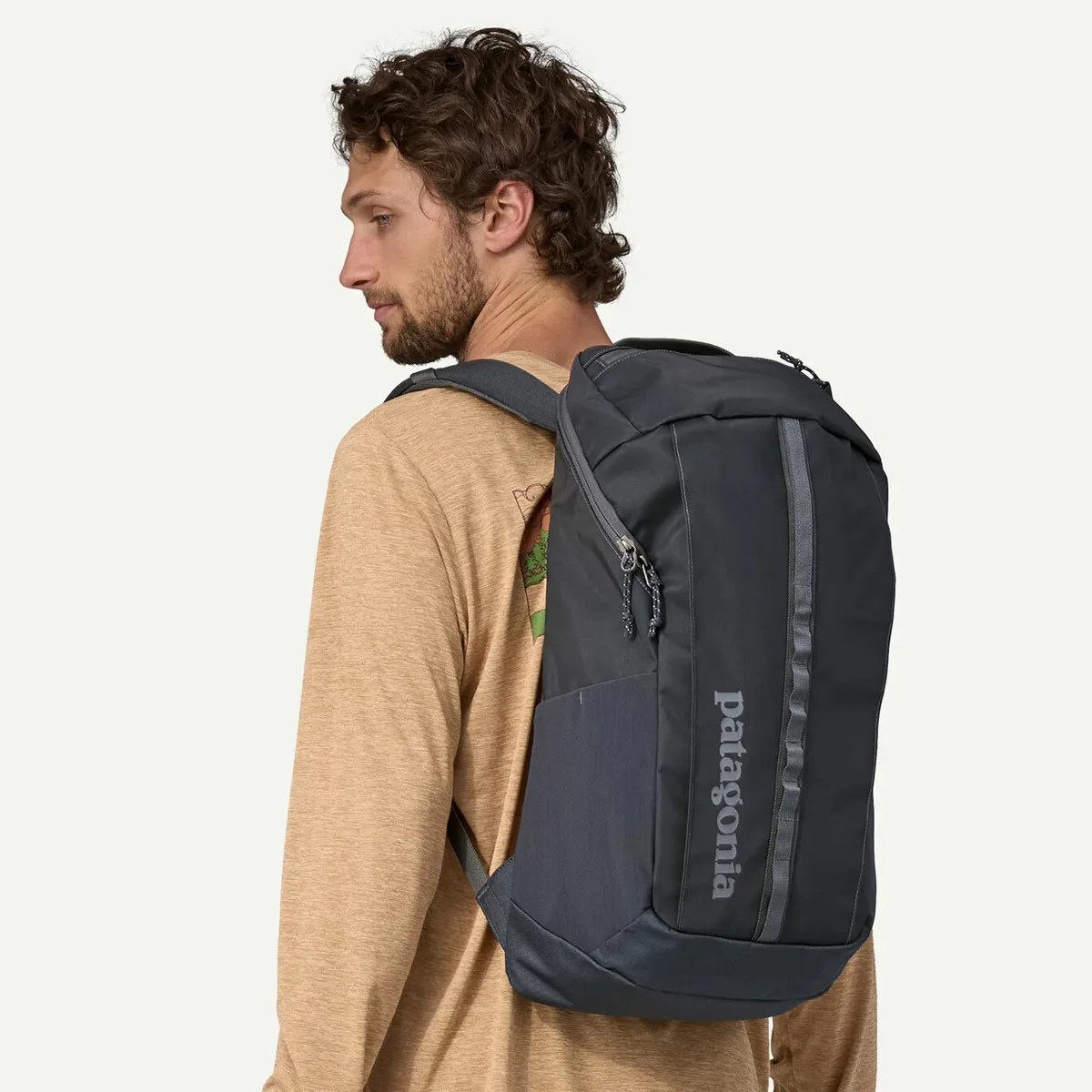 Black Patagonia backpack with vertical logo worn by a person in a tan long-sleeve shirt.