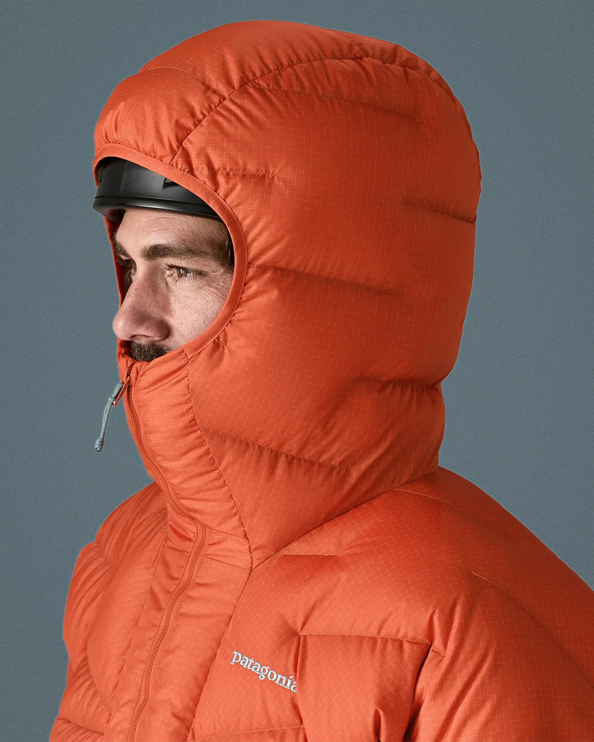 Orange Patagonia insulated hooded jacket worn over a black helmet on a person facing left.
